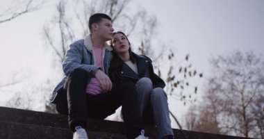 Genç bir çift parkta basamaklarda oturuyor, birbirlerine eşlik ediyorlar ve manzarayı izliyorlar..