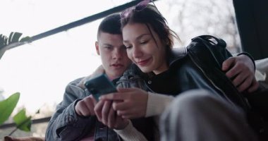 Genç bir çift birlikte oturur, akıllı telefonlara göz atar ve selfie çekerler. Mutlu ve bağlı görünüyorlar..