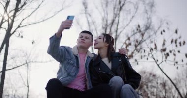 Genç bir çift selfie çeker ve parkta hassas bir anı paylaşır. Birbirlerine eşlik etmekten, fotoğraf çekmekten ve içeriği taramaktan hoşlanırlar..