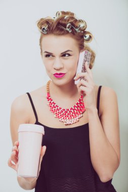 Cep telefonu evde kullanan genç kadın. Onun el ve saçında curlers içecekler.