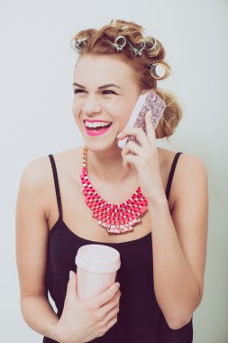 Cep telefonu evde kullanan genç kadın. Onun el ve saçında curlers içecekler.