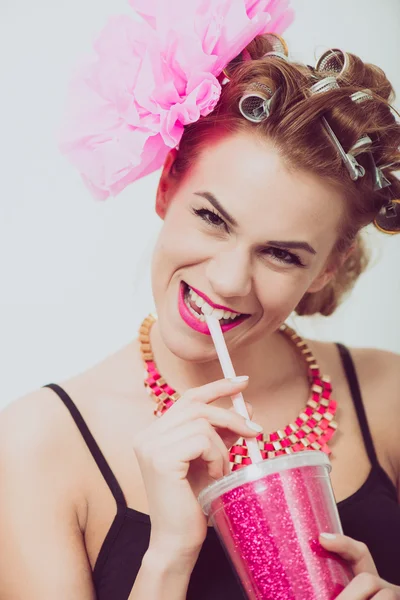 Felice, giovane donna che beve, usando una cannuccia. bigodini sui capelli . — Foto Stock