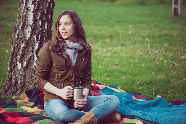 Ung brunett kvinna vila under ett träd under resan. Kaukasiska backpacker kvinna med en mugg utomhus. — Stockfoto