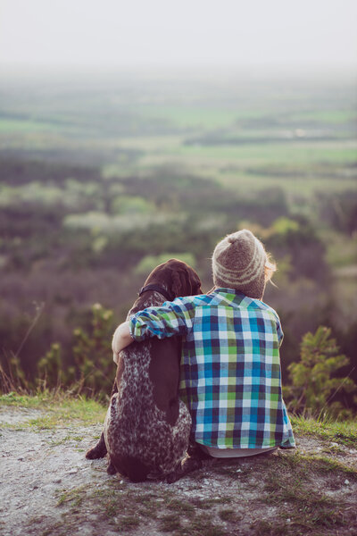 Женщина и ее собака позируют на улице. Девушка любит и крепко обнимает свою собаку и смотрит пейзаж
.