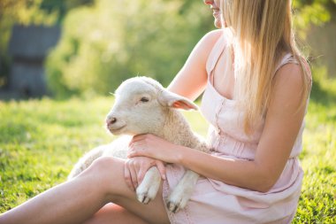 Çiftçi kadın tarafından bakımı sevimli, genç kuzu yakın görüntü. Mutlu kadın gülümseyen ve sevimli bir kuzu tutan.