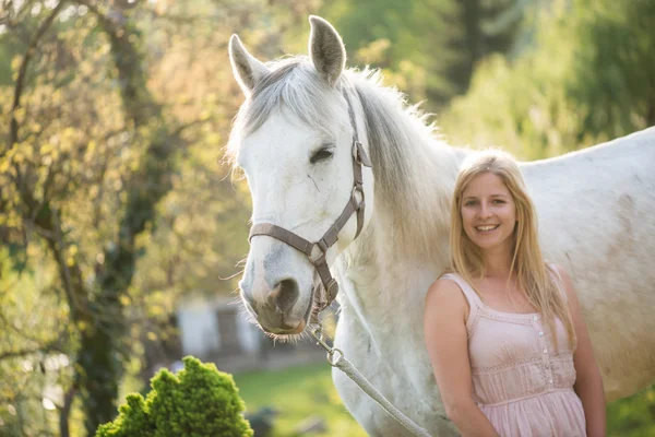 Jovem loira posando ao ar livre com cavalo branco . — Fotografia de Stock