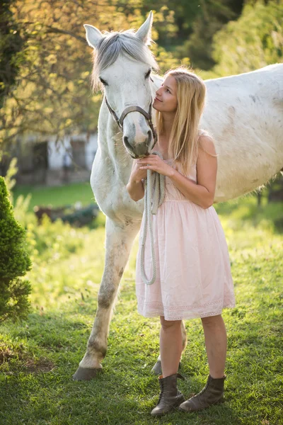 Junge blonde Frau posiert im Freien mit weißen Pferd. — Stockfoto