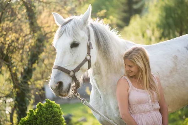 Jonge blonde vrouw poseren buiten met wit paard. — Stockfoto