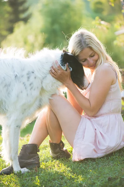 Щаслива блондинка грає з її Російська собака вовкодав в саду — стокове фото