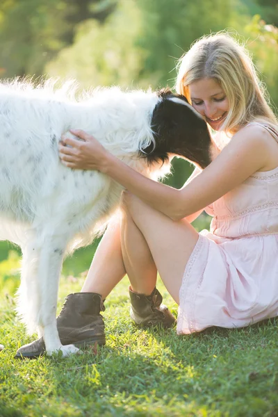 Glückliche blonde Frau spielt mit ihrem russischen Wolfshund im Garten — Stockfoto