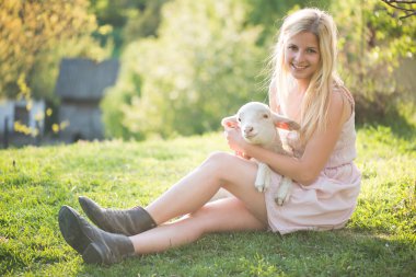 Çiftçi kadın tarafından bakımı sevimli, genç kuzu yakın görüntü. Mutlu kadın gülümseyen ve sevimli bir kuzu tutan.