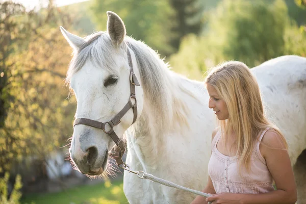 Mladá blondýnka pózuje venkovní s bílým koněm. — Stock fotografie