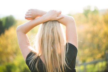 Sarışın kadın günbatımında açık poz. Manzara izlerken. Kollarını kaldır.