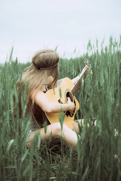 Young woman sitting on a field and playing guitar — Stock Photo, Image