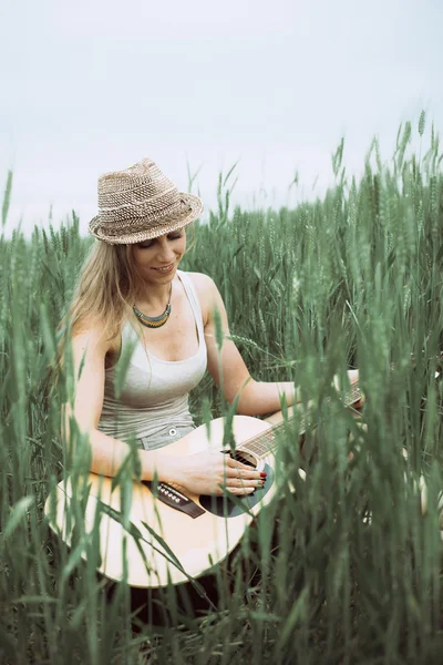 Junge Frau sitzt auf einem Feld und spielt Gitarre — Stockfoto