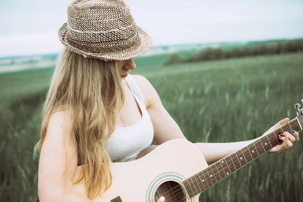 Young woman sitting on a field and playing guitar — Stock Photo, Image