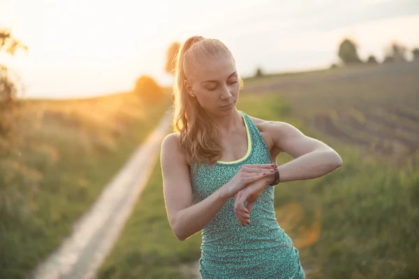 Genç kadın jogger set ve spor akıllı bakarak, performans veya nabız nabız izleme kontrol çalışmaya hazır. Spor ve fitness açık — Stok fotoğraf