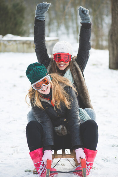 Laughing girls sledge downhill in wintertime enjoy snow