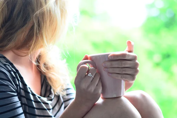 Cute blonde sitting on the windowsill and looking out the window with cup of coffee in the morning — Stock Photo, Image