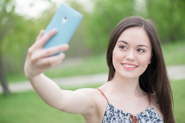 Akıllı telefon kullanarak kendi kendine portre alarak gülümseyen Asyalı kız
