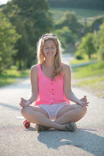 Blonde skateboarder faire du yoga en plein air — Photo