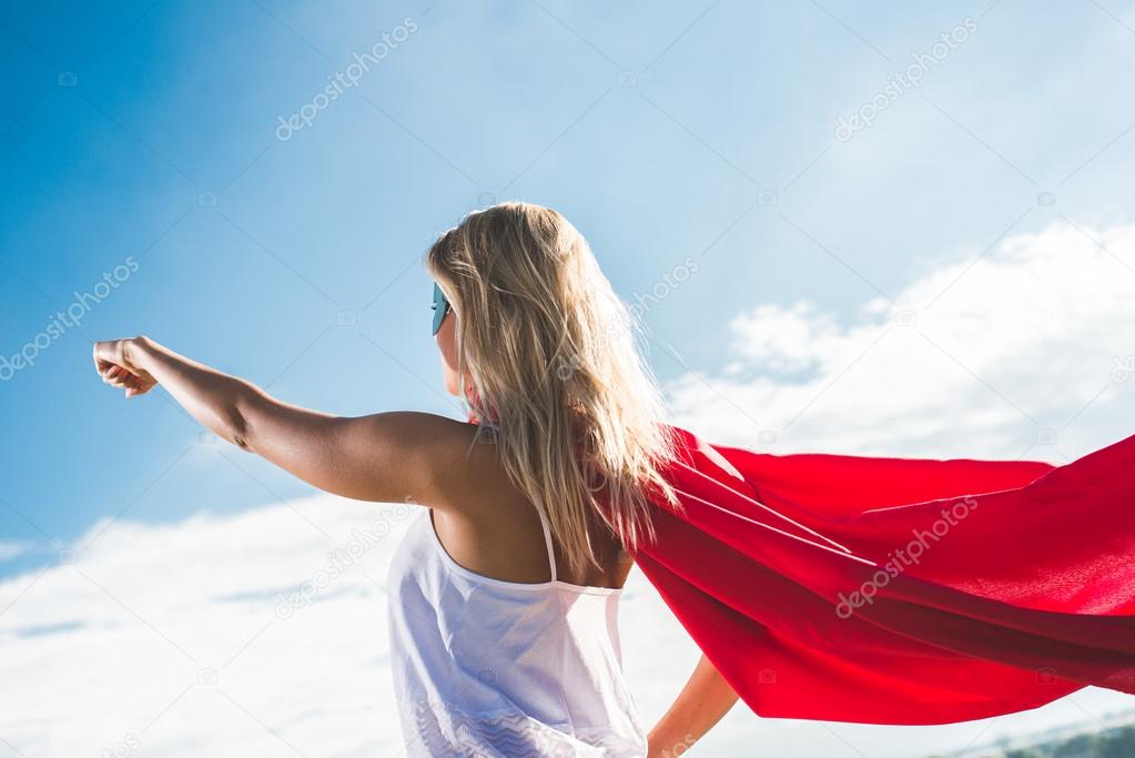 Young woman posing as superhero over blue sky