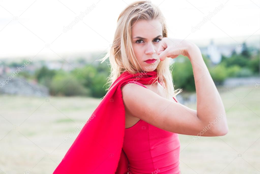 Confident blonde woman in red costume showing muscle and strength