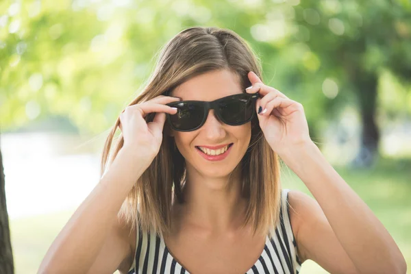 Літній портрет молодої брюнетки, яка грає зі своїми сонцезахисними окулярами і розважається на відкритому повітрі — стокове фото