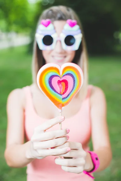 Beautiful young woman is holding lollipop in front of her mouth while standing — Stock Photo, Image