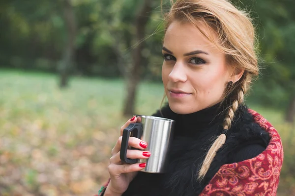 Mladá žena pít horký čaj nebo kávu venkovní v podzimním parku — Stock fotografie