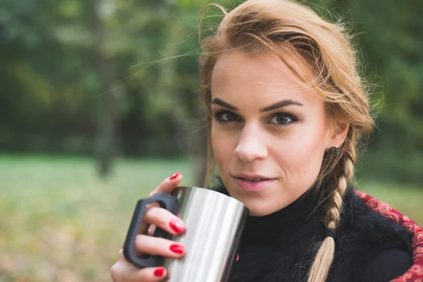 Mladá žena pít horký čaj nebo kávu venkovní v podzimním parku — Stock fotografie
