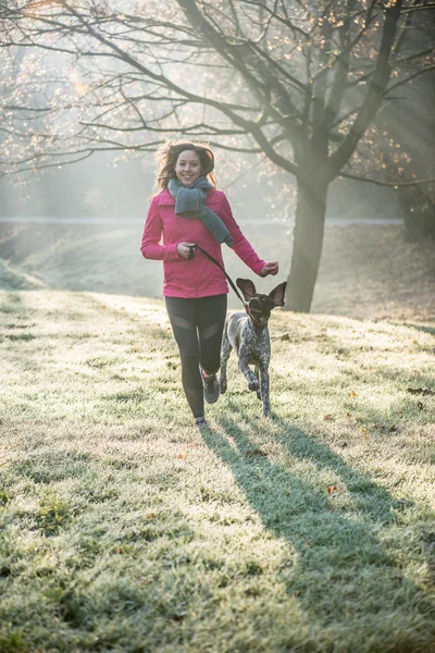 Runner mulher e seu bonito cão ponteiro alemão correndo juntos ao ar livre no belo parque . — Fotografia de Stock