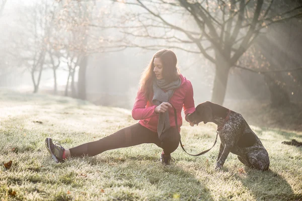 Vrouw en haar hond stretching buiten. Fitness meisje en haar huisdier uit samen te werken. — Stockfoto