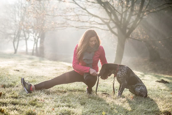 Žena a její pes táhne venkovní. Fitness dívka a její mazlíček cvičit společně. — Stock fotografie