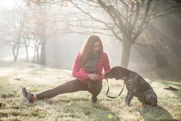 Mulher e seu cão se esticando ao ar livre. Fitness menina e seu animal de estimação trabalhando juntos . — Fotografia de Stock