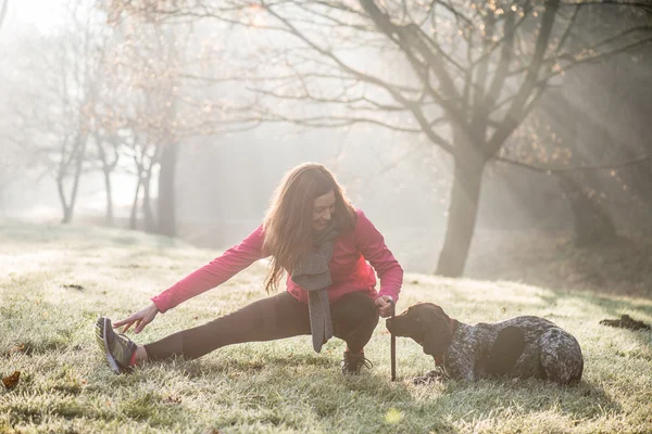 Mujer y su perro estirándose al aire libre. Chica de fitness y su mascota haciendo ejercicio juntos . —  Fotos de Stock