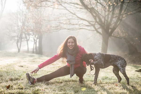 Γυναίκα και το σκυλί τέντωμα υπαίθρια. Κορίτσι Fitness και το κατοικίδιο ζώο που εργάζονται έξω μαζί. — Φωτογραφία Αρχείου