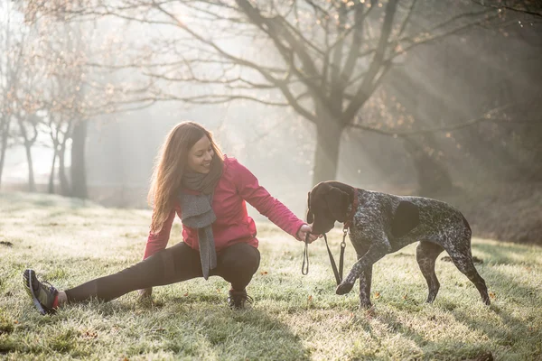 Kvinna och hennes hund sträcker sig utomhus. Fitness flicka och hennes husdjur träna tillsammans. — Stockfoto
