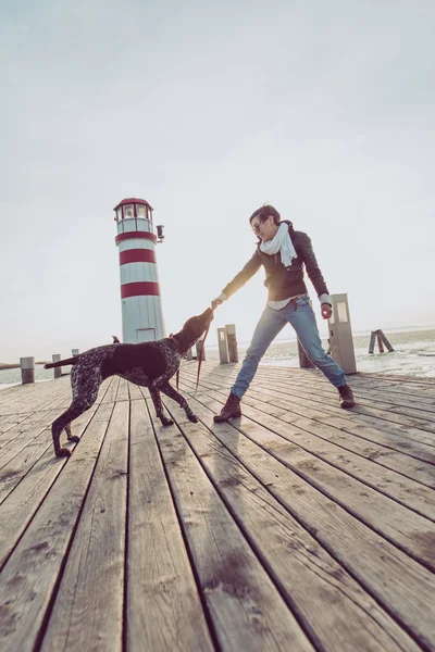 Vacker ung kvinna leker med hunden på havsstranden — Stockfoto