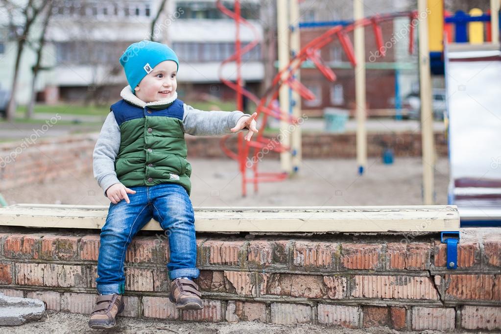 Мальчик на спортивной площадке. Cute little boy squatting on his haunches on the Playground. Isolated on White background.