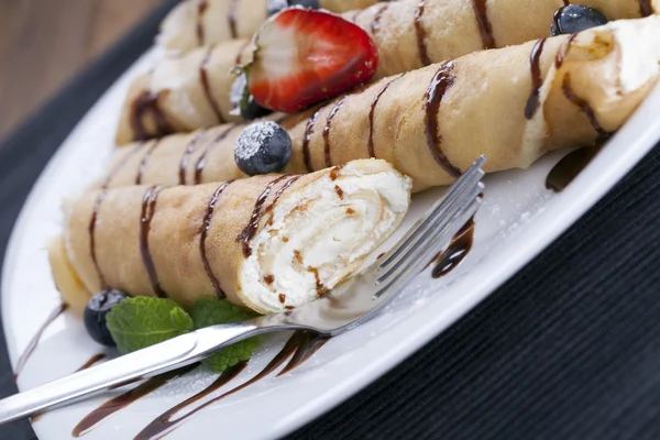 Delicious sweet rolled pancakes on a plate with fresh fruits — Stock Photo, Image