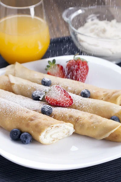 Deliciosos panqueques dulces enrollados en un plato con frutas frescas — Foto de Stock