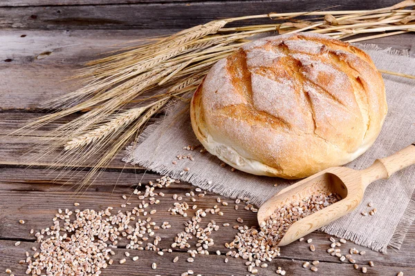 Pão caseiro e orelhas maduras de trigo em um fundo de madeira — Fotografia de Stock