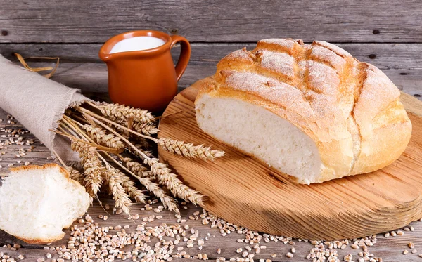 Pão caseiro, leite e orelhas maduras de centeio em um fundo de madeira — Fotografia de Stock