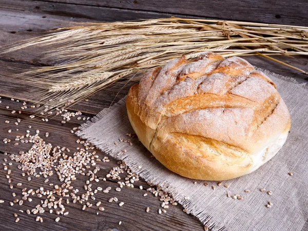 Pão caseiro e orelhas maduras de trigo em um fundo de madeira — Fotografia de Stock