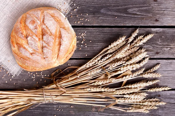 Pão caseiro e orelhas maduras de centeio em um fundo de madeira — Fotografia de Stock