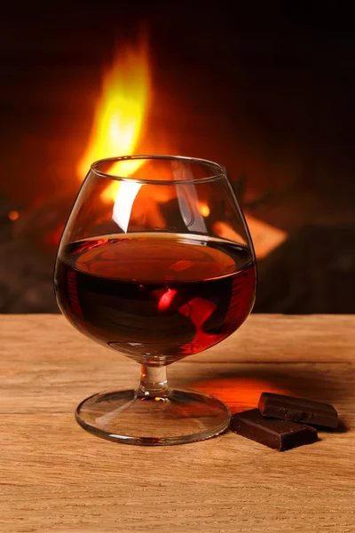 A glass of cognac and chocolate  on the background of a burning — Stock Photo, Image