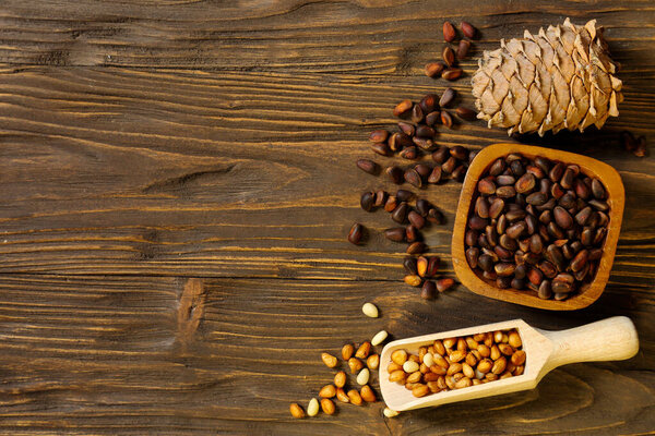 Pine nuts in a bowl and pine cone on a wooden background, place for text 