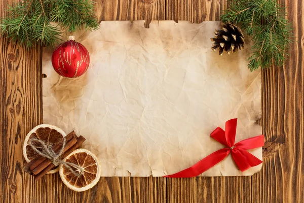 Las decoraciones navideñas en la hoja vieja del papel sobre la espalda de madera —  Fotos de Stock