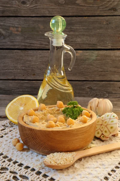 Hummus in een houten kom en ingrediënten aan het koken — Stockfoto